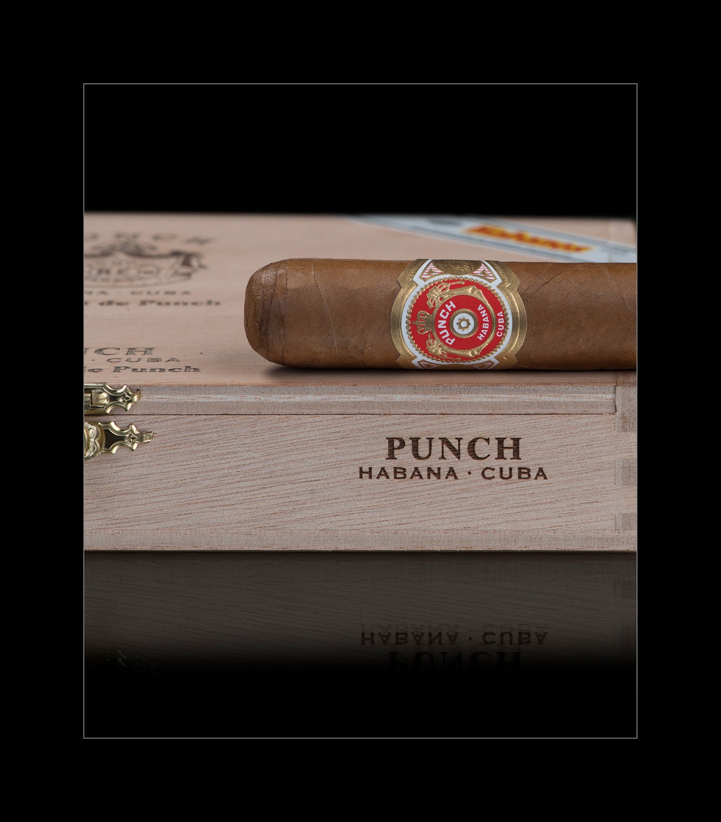 A single cigar resting horizontally on top of a wooden box engraved with 'PUNCH HABANA - CUBA'. The cigar has a brown wrapper and a red, white, and gold band.