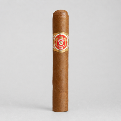 A single brown cigar standing upright on a light gray background, featuring a red and gold Tunica band label around the middle.