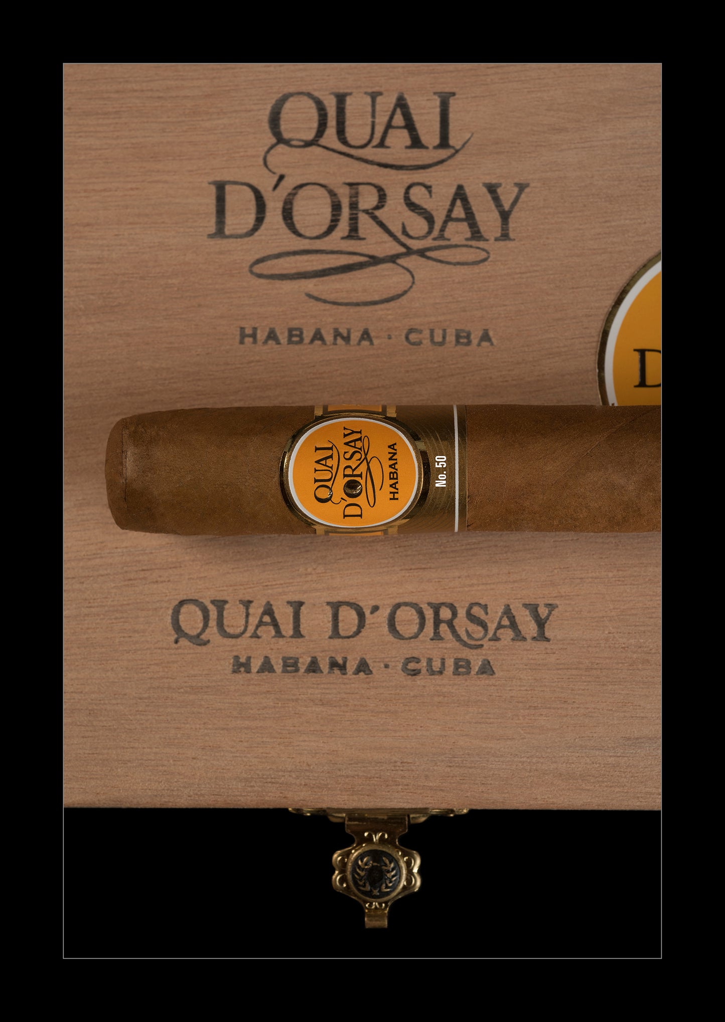 A single cigar resting horizontally on a branded wooden box lid, with the Quai D'Orsay Habana - Cuba branding visible above and below. The cigar has a gold and black band label, and the box is shown against a black background.