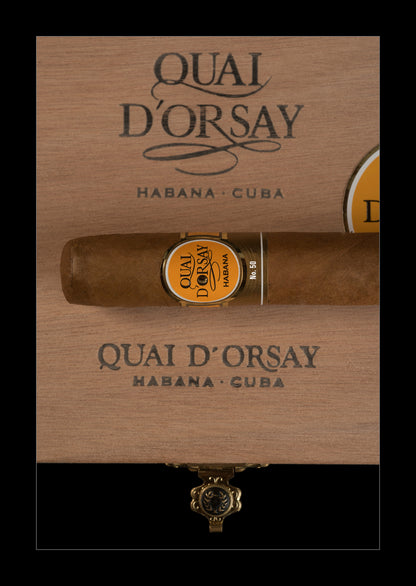 A single cigar resting horizontally on a branded wooden box lid, with the Quai D'Orsay Habana - Cuba branding visible above and below. The cigar has a gold and black band label, and the box is shown against a black background.