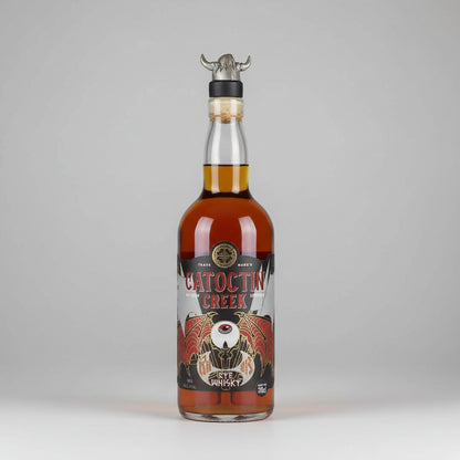 A bottle of Catocin Creek ragnok Whiskey with amber liquid, a black and red label, and a metal horn stopper on a white background.