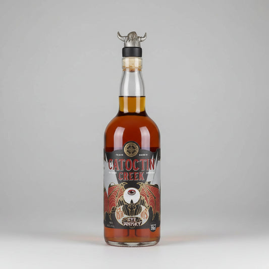 A bottle of Catocin Creek ragnok Whiskey with amber liquid, a black and red label, and a metal horn stopper on a white background.