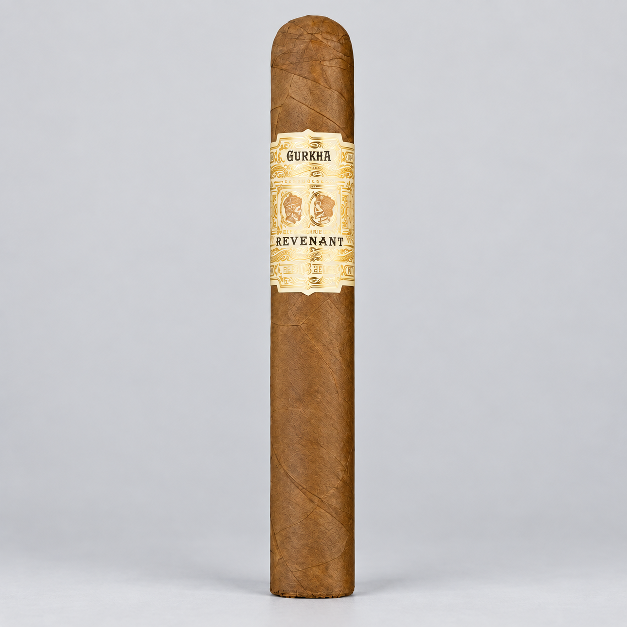 A single brown cigar standing upright against a light gray studio background, featuring a cream and gold band labeled 'GURKAA' and 'REVENANT'.