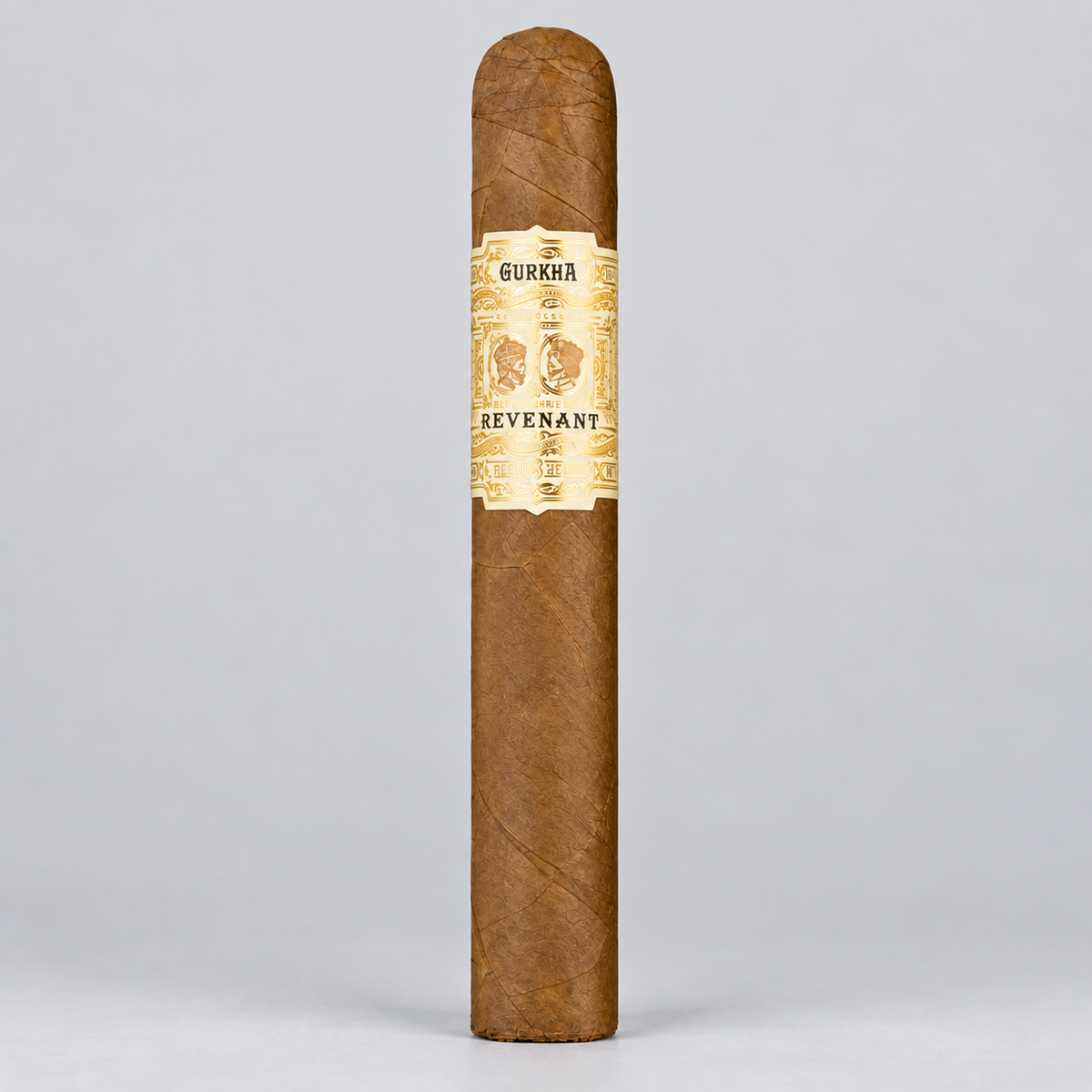 A single brown cigar standing upright against a light gray studio background, featuring a cream and gold band labeled 'GURKAA' and 'REVENANT'.