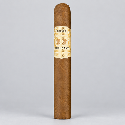 A single brown cigar standing upright against a light gray studio background, featuring a cream and gold band labeled 'GURKAA' and 'REVENANT'.