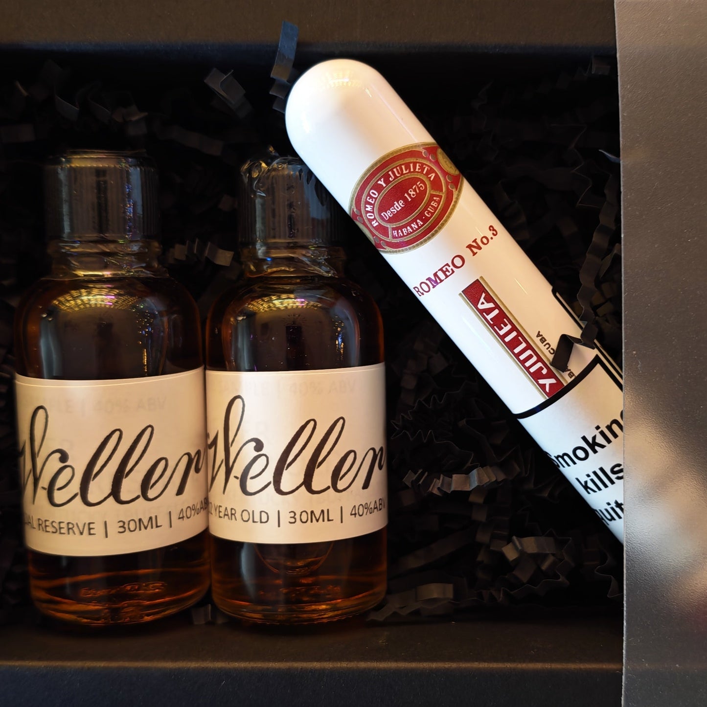 Two bottles of Weller bourbon and a Romeo Y Juliet No.3 cigar in a black box on a white background 