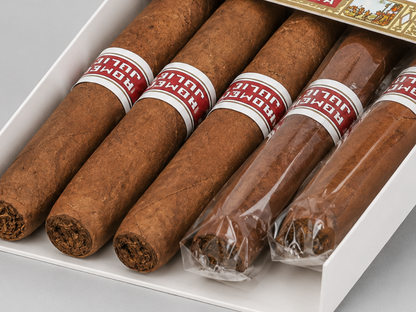 A white box of Romeo y Julieta cigars on a light gray background, with four unsealed cigars showing their brown wrappers and two sealed cigars wrapped in clear plastic under red and white bands.