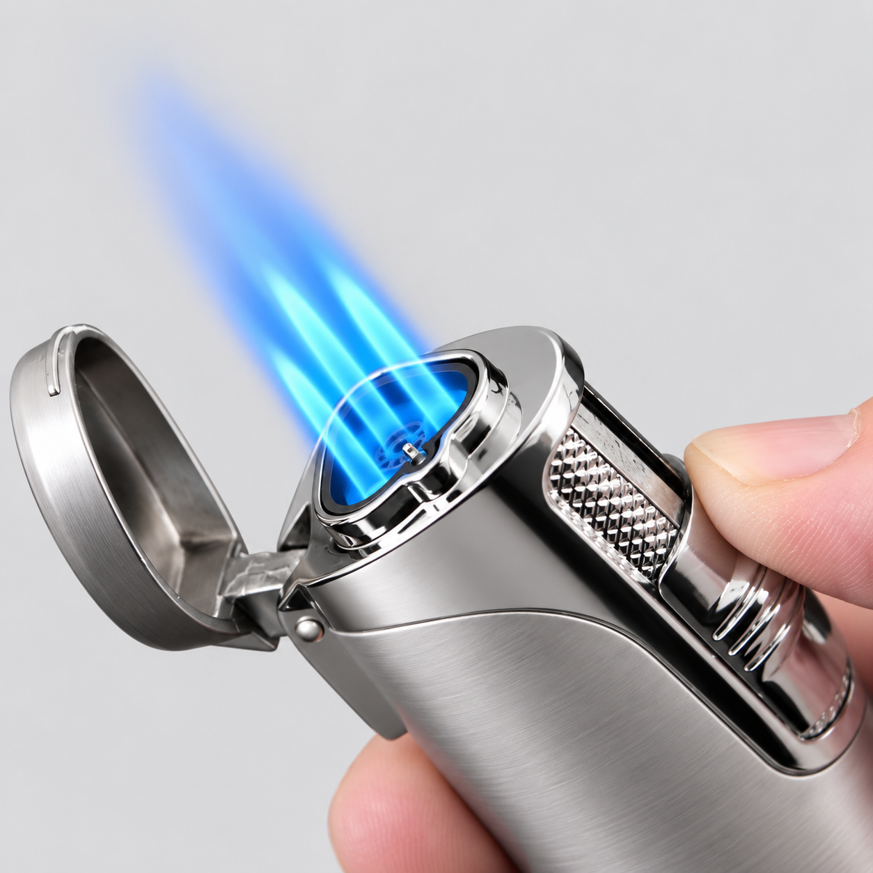A close-up of a silver metal torch lighter being held by a hand, with its lid open and a bright blue flame ignited against a light gray background.