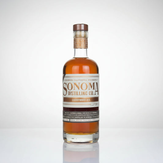 A bottle of Sonoma Distilling Co. Cherrywood Rye whiskey, showing the amber liquid inside a clear glass bottle with a cream and brown label, set against a plain white background with a soft reflection below.