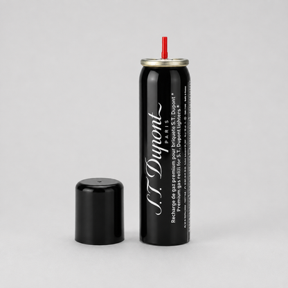 A black aerosol can with a silver top and red nozzle, shown next to its detached black cap on a light gray background. The can features the brand name 'S.