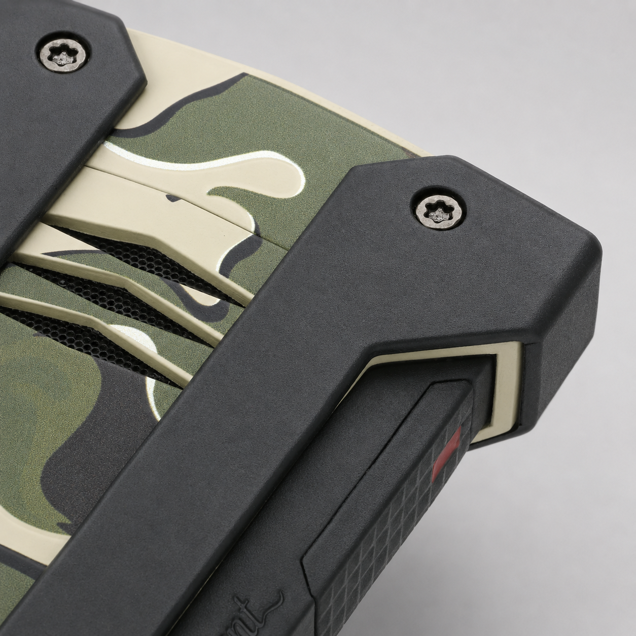 Close-up of a rugged dupont lighter corner showing a black protective frame, screws, mesh vents, and a green, beige, and black camouflage pattern on a light gray background.
