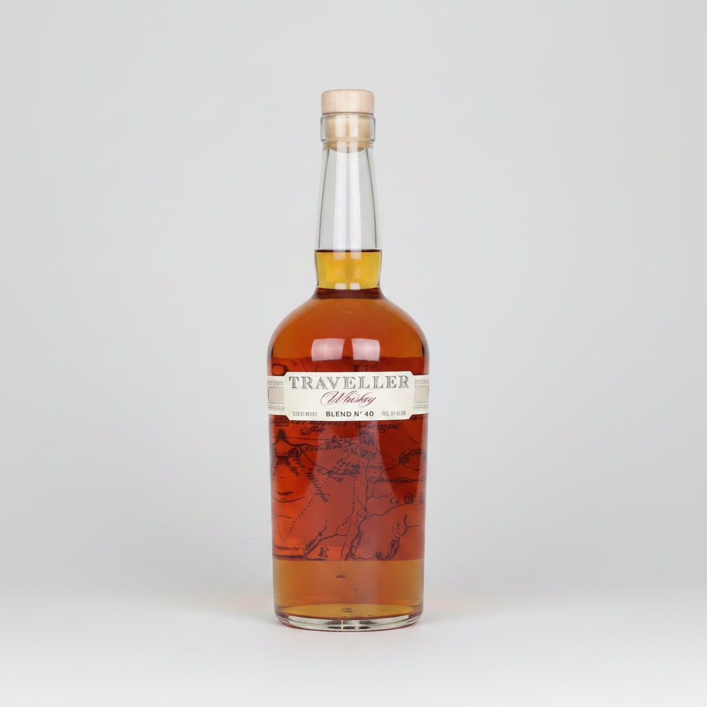 A bottle of Traveller Whiskey Blend No. 40 on a white background, showing the amber liquid inside a clear glass bottle with a cream-colored label and cork stopper.