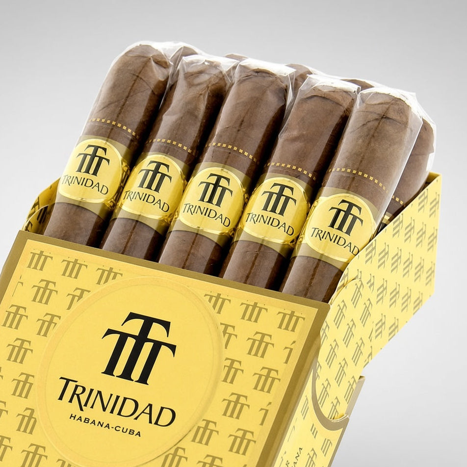 A box of Trinidad cigars with five cigars visible in the top slot, set against a clean light gray background. The packaging is gold and yellow with black branding, and the cigars are wrapped in brown paper with matching gold bands.