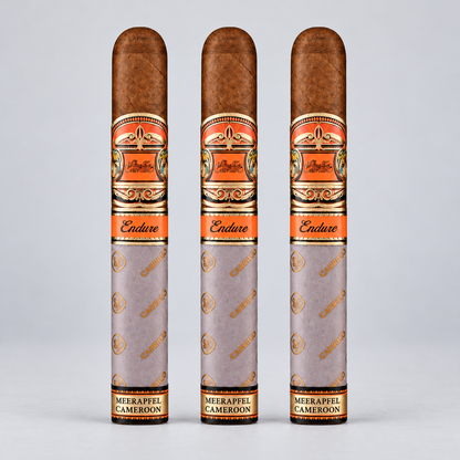 Three cigar tubes standing upright on a light gray background. The tubes are light gray with gold and orange decorative bands and the brand name 'Endure' is visible on the orange bands.