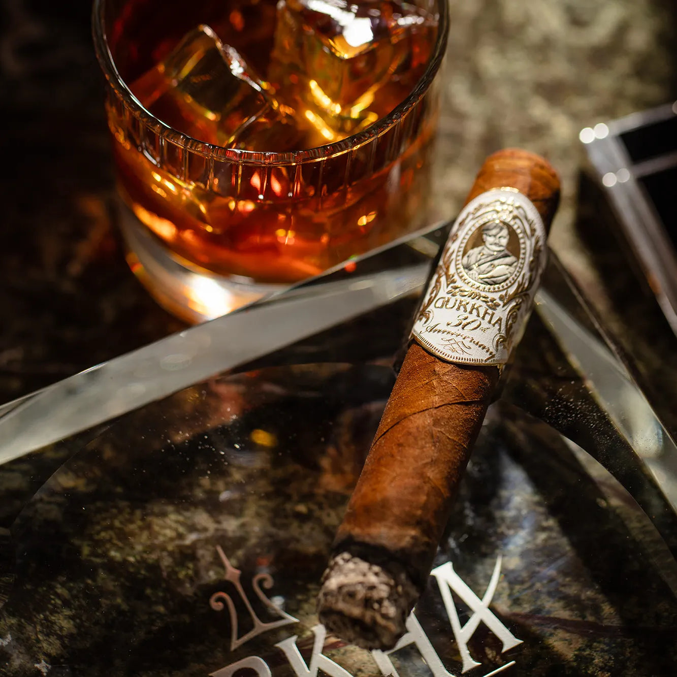 Cigar with a band and glass of whiskey on a dark surface