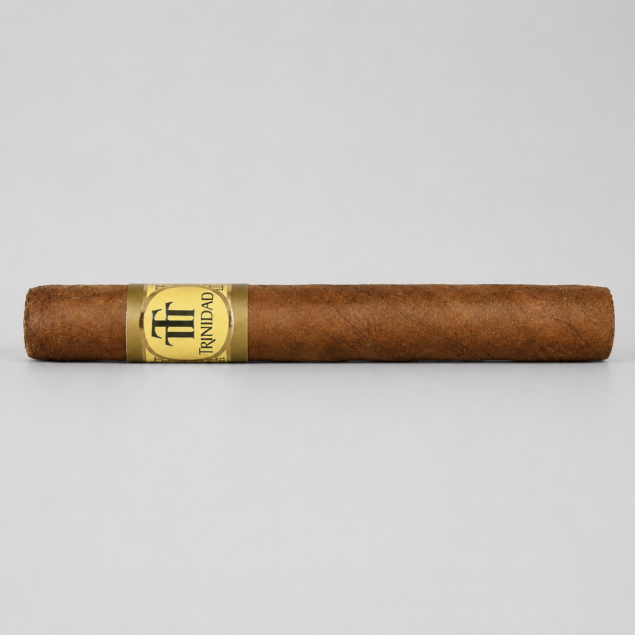A single brown cigar with a gold and black Triunfo band, photographed horizontally against a neutral light gray background.