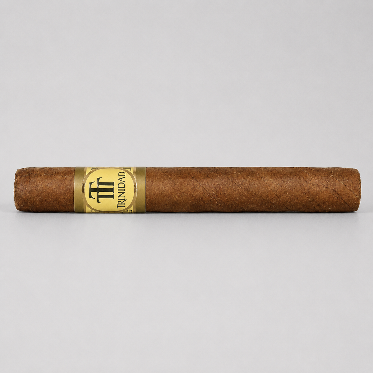 A single brown cigar with a gold and black Triunfo band, photographed horizontally against a neutral light gray background.