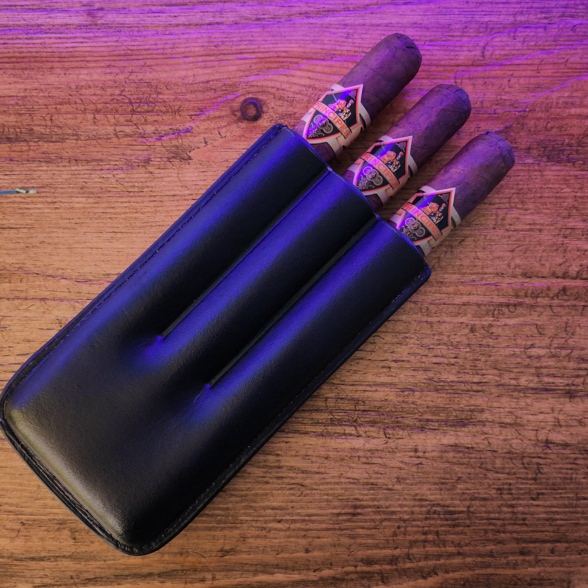 Three cigars in a black humidor on a wooden surface