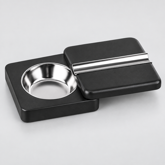 A black rectangular cigar holder with a circular stainless steel bowl on one side and a matching lid on top featuring a silver metal accent bar, shown on a light gray background.