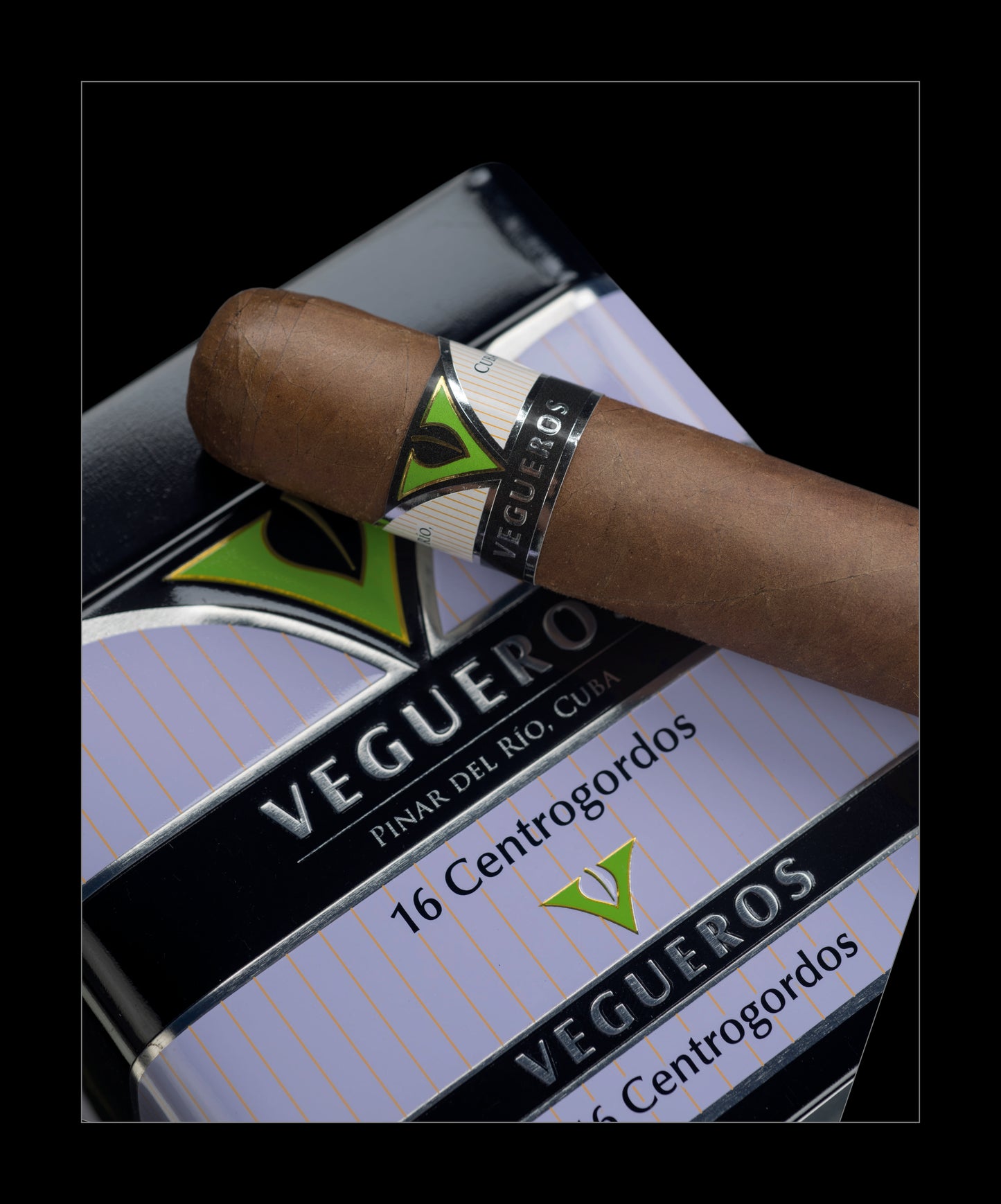 A single cigar with a silver and green Vegueros band resting diagonally across a Vegueros pack on a black background.