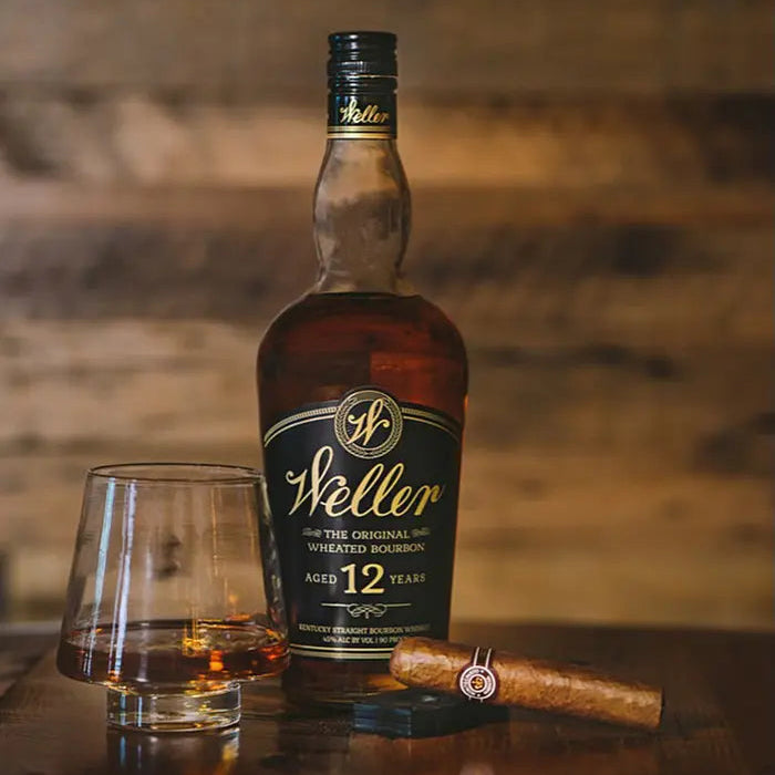 Weller 12-year-old bourbon bottle with a glass and a cigar on a wooden surface.