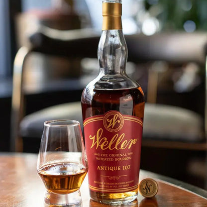 Weller whiskey bottle with a glass of whiskey on a wooden table.