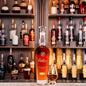 Weller whiskey bottle with a glass on a bar shelf with various bottles in the background