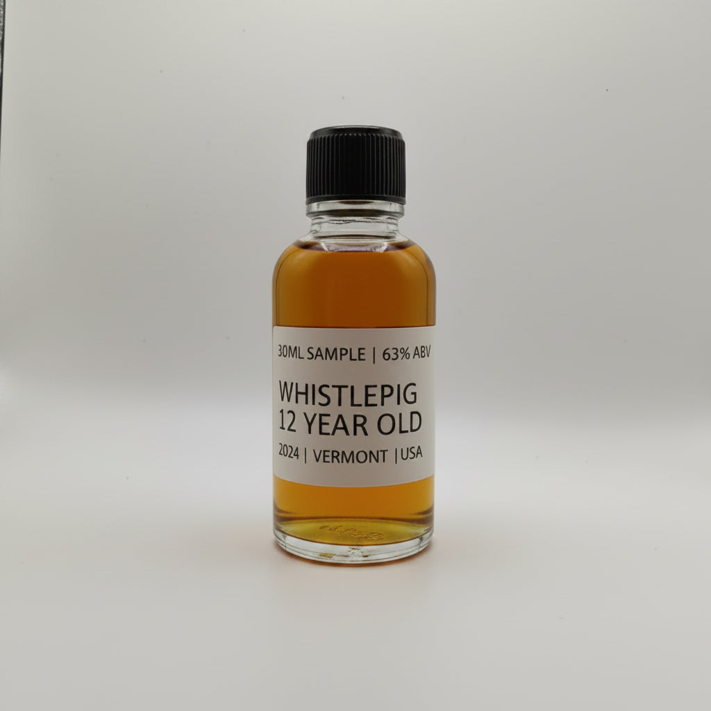 Small bottle of WhistlePig 12 Year Old whiskey sample on a white surface with a gray leather chair in the background.