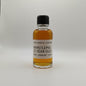 Small bottle of WhistlePig 12 Year Old whiskey sample on a white surface with a gray leather chair in the background.