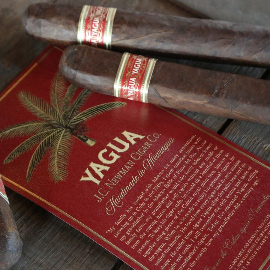Two Yagua cigars with red and gold bands resting on a red branded cigar box, photographed on a rustic wooden surface.