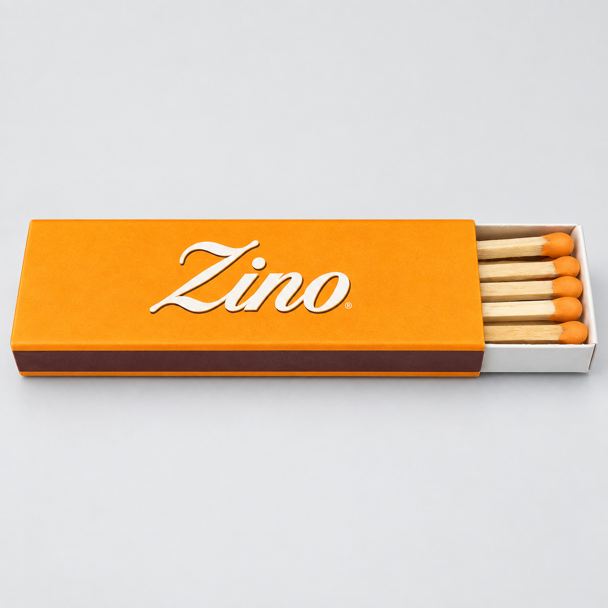 An orange matchbox with the brand name 'Zino' in white script, shown open with several wooden matches and orange tips on a light gray background.