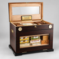 A premium humidor and cigar storage cabinet with a dark wood grain exterior, open top, and glass-front lower compartment displaying cigars and boxes, photographed on a light gray studio background.