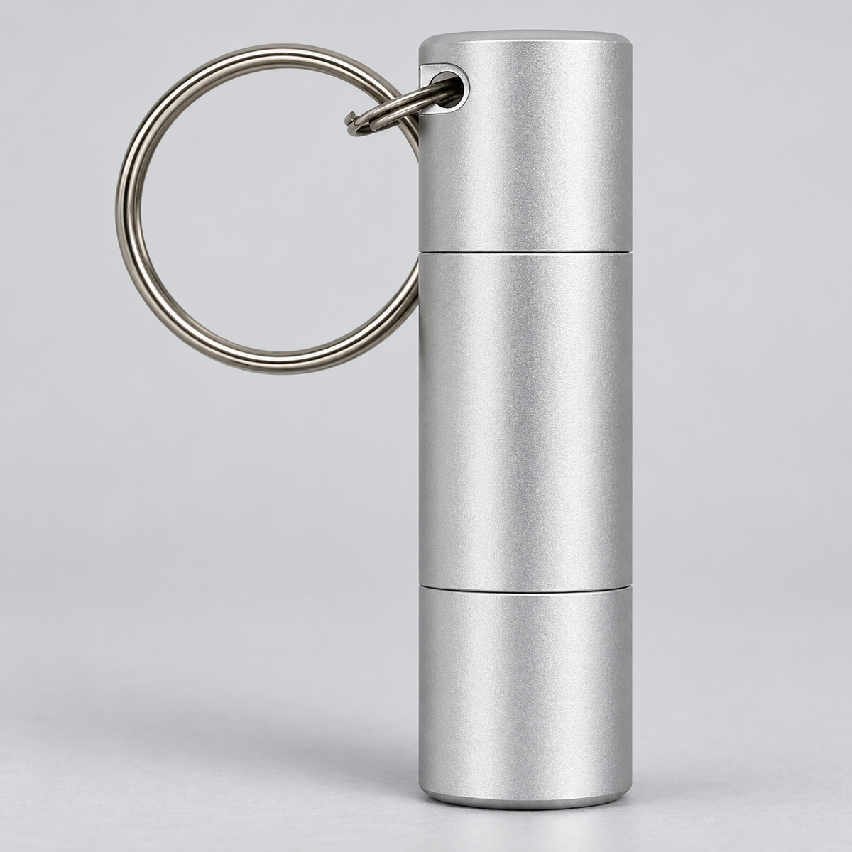A silver metallic cylindrical keychain container with a split ring, shown on a light gray studio background.