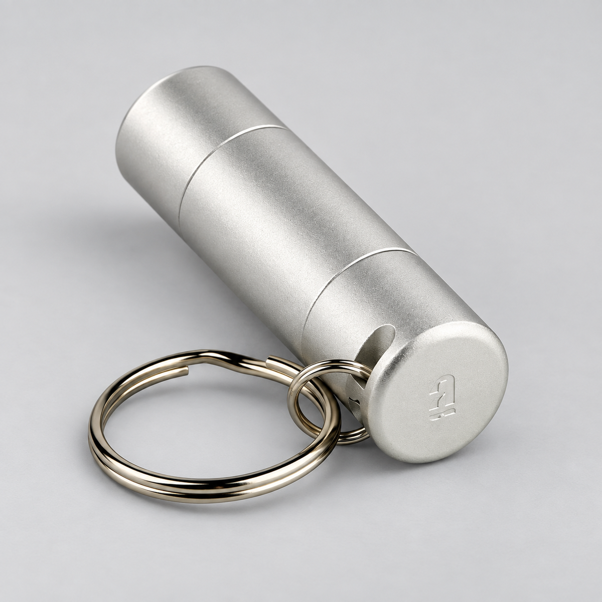 A silver cylindrical metal keychain container with a matching split key ring, photographed on a clean light gray background.