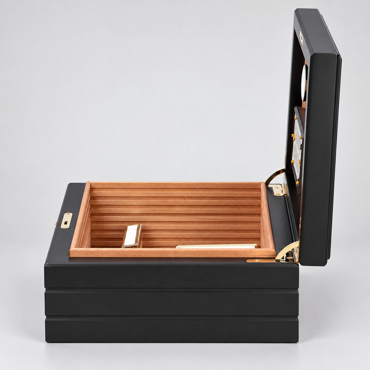 A luxury cigar humidor box with a black lacquered exterior, a warm natural wood interior, and gold-tone metal hardware, shown open against a light gray background.