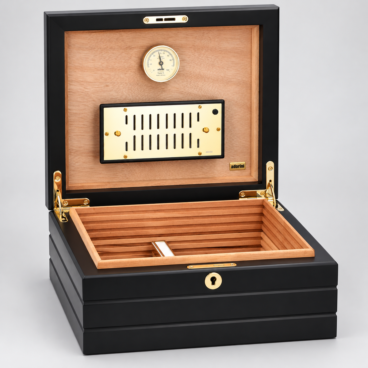 A luxury humidor box with a black lacquered exterior, a light natural wood interior, and gold-tone hardware, shown open against a neutral gray background.