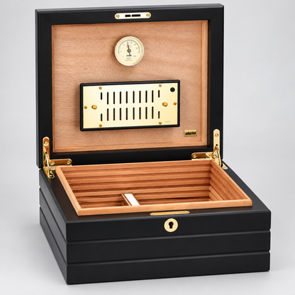 A luxury humidor box with a black lacquered exterior, a light natural wood interior, and gold-tone hardware, shown open against a neutral gray background.