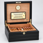 An open black humidor box with a natural wood interior, displaying cigars in a wooden tray, a hygrometer, and a humidifier panel. The brand name 'Mori' is visible on the humidifier plate.