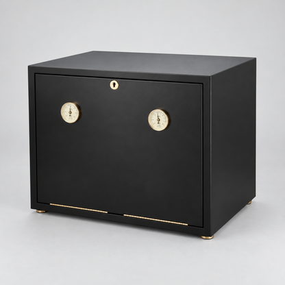 A matte black humidor safe with two round brass dials and a small brass lock keyhole on the front door, standing on small brass feet against a light gray studio background.
