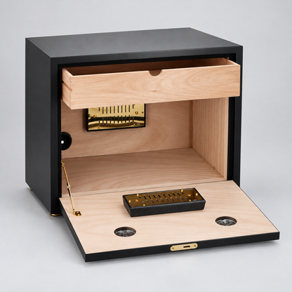 A black wooden humidor with its drawer and front door open, showing a light natural wood interior, brass-toned humidor mechanism, and small black accessory tray on a light gray background.