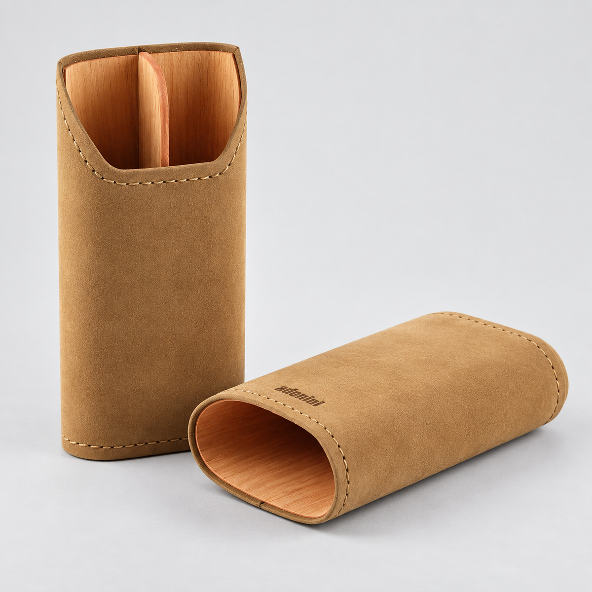 Two tan suede-like cylindrical cases with visible wood interiors and stitched edges, photographed on a clean light gray studio background. One case is upright and open, and the other lies on its side showing the interior.
