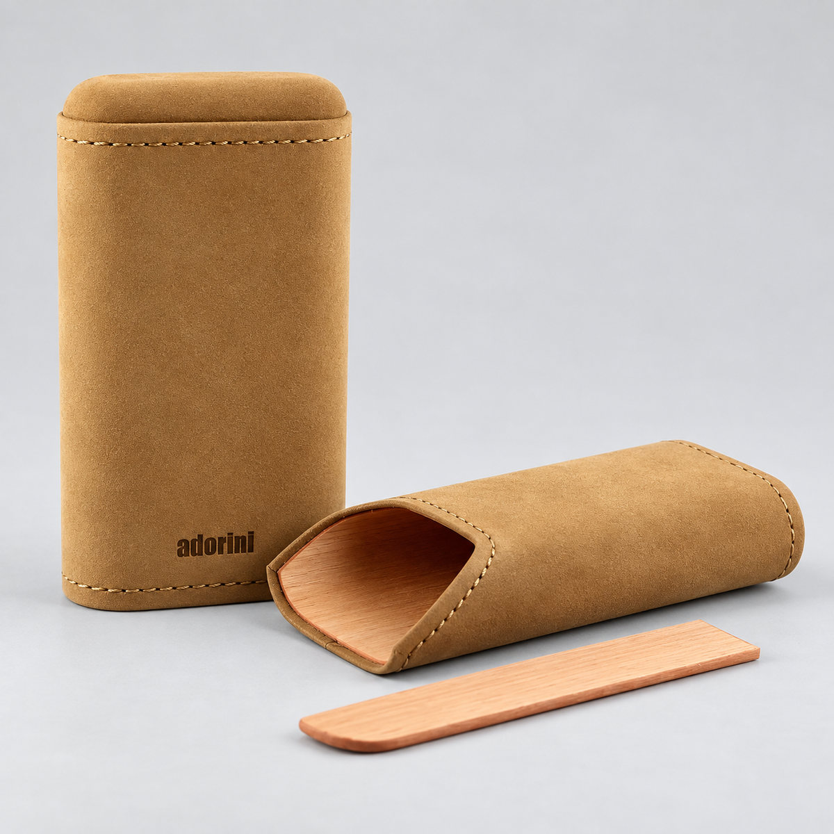 A tan suede-like cylindrical case with a small wooden stick, shown alongside another case standing upright. The standing case has the brand name 'adorim' printed in black near the bottom.