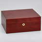 A rectangular wooden storage box with a glossy reddish-brown wood grain finish and a small round gold-tone keyhole detail on the front, photographed on a light gray studio background.