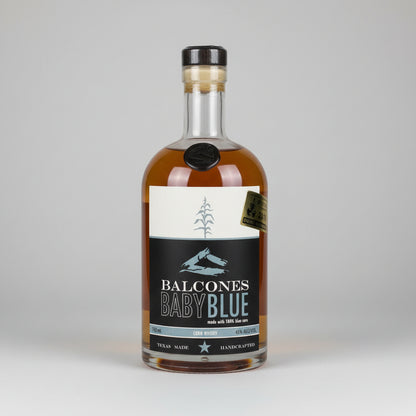 A bottle of Balcones Baby Blue bourbon whiskey against a white background, featuring a black and white label with a pine tree graphic.