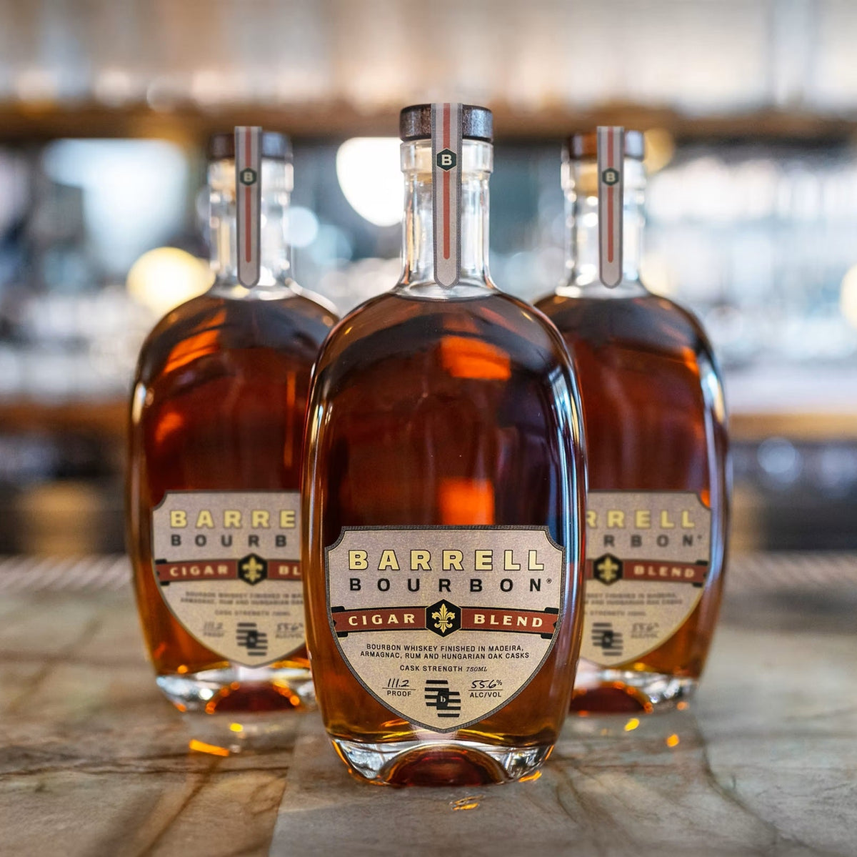 Three bottles of Barrel Bourbon Cigar Blend bourbon whiskey arranged on a bar counter with a blurred bar background.