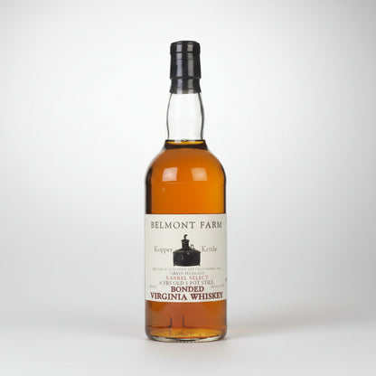 A bottle of Belmont Farm Kopper Kettle Virginia Whiskey, showing the amber liquid inside a clear glass bottle with a black cap and a white label.
