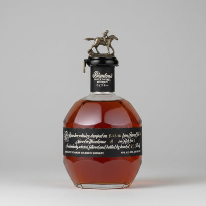 A bottle of Blanton's Single Barrel Bourbon Whiskey with a black label and a silver horse-and-rider cap, shown against a neutral gray background.