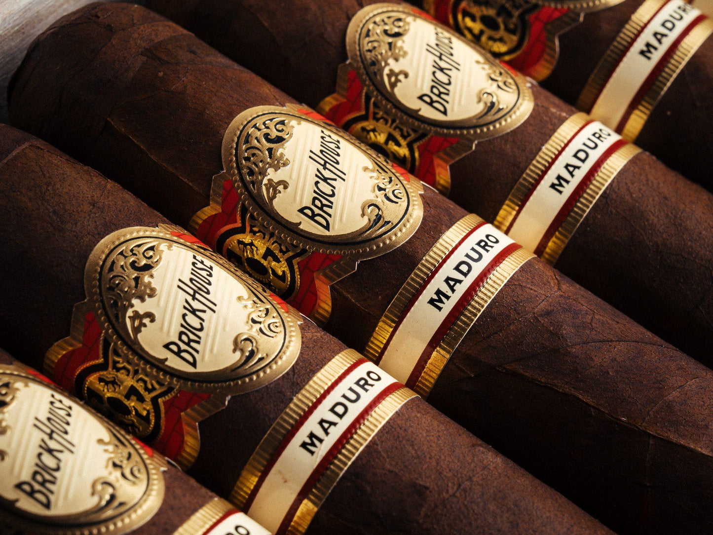 Close-up of several dark brown cigars arranged diagonally, each with a white and gold Brackhouse label and a white MADURO band.