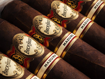 Close-up of several dark brown cigars arranged diagonally, each with a white and gold Brackhouse label and a white MADURO band.