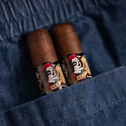 Two brown cigars with decorative bands featuring a skull illustration and the text 'Cigar del Rey', resting in a blue denim pocket.